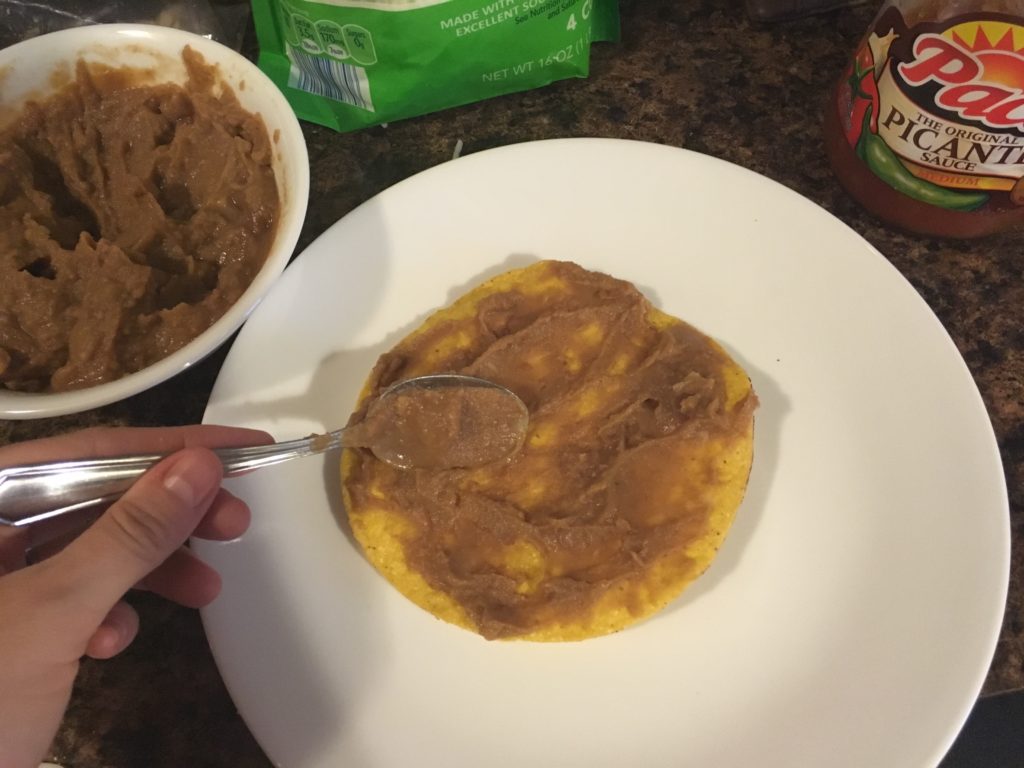 spreading refried beans on a tostada