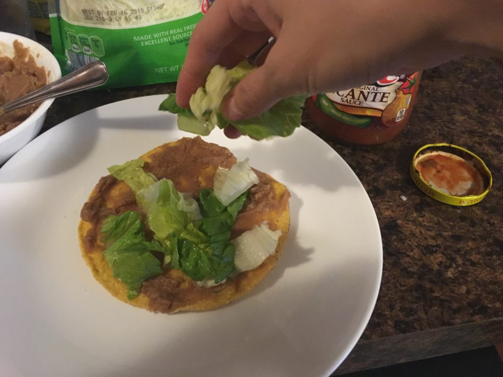 adding lettuce to a tostada