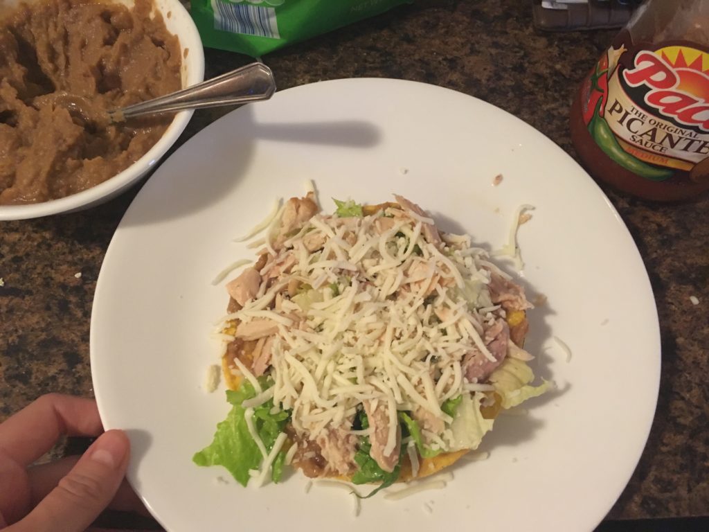 tostada topped with beans, lettuce, chicken, and cheese