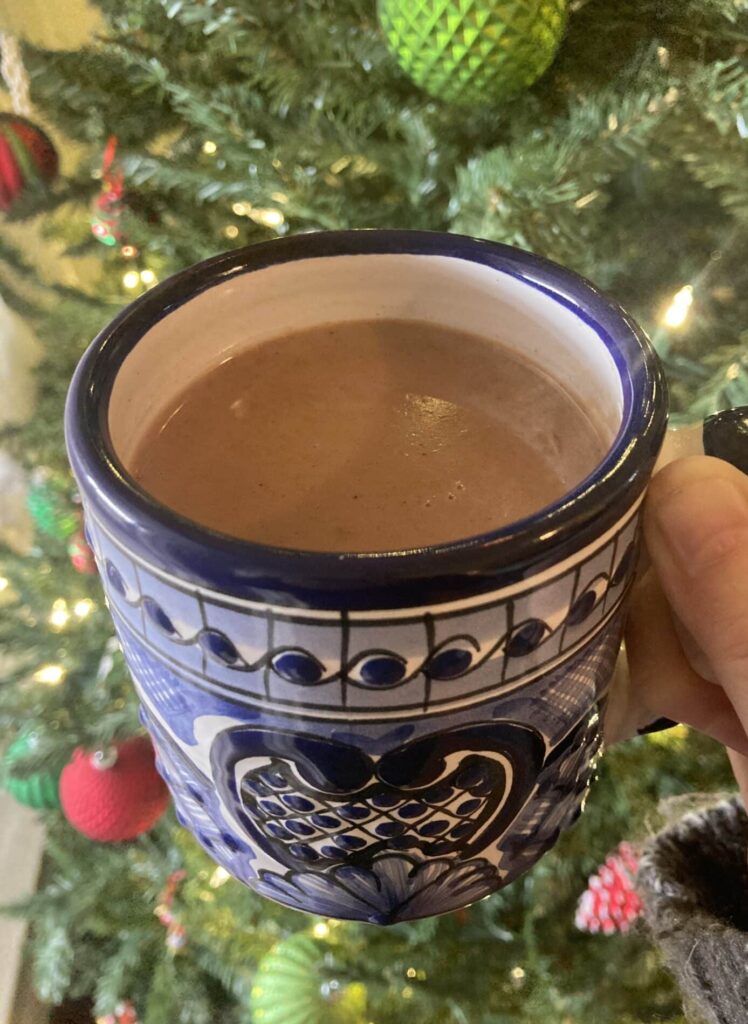 Champurrado - thick Mexican hot chocolate - in a mug by a Christmas tree.